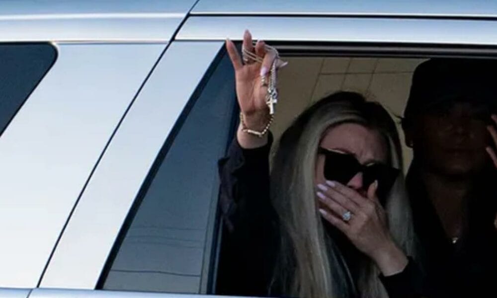 Erika Kirk waves to supporters holding Charlie Kirk’s cross necklace, a symbol of his faith and enduring legacy.