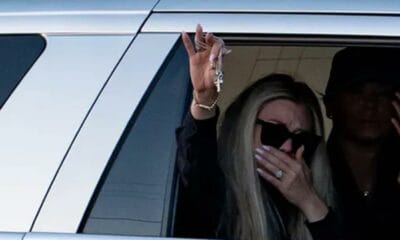 Erika Kirk waves to supporters holding Charlie Kirk’s cross necklace, a symbol of his faith and enduring legacy.